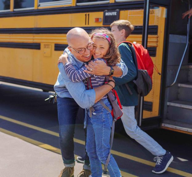 A man hugs a child as they get off a school bus. 